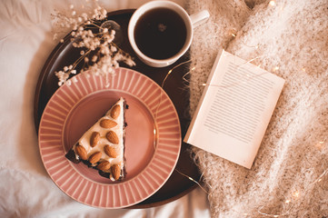 Tasty breakfast in bed with open book on knitted cloth closeup. Top view. Warm winter evening.