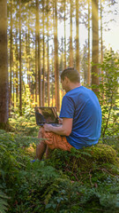 Fototapeta premium Healthy work life balance - working with a laptop in a green sunny forest.