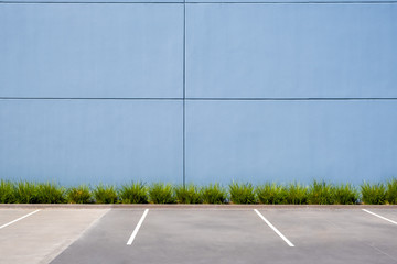 Empty parking spaces against clean concrete wall of an industrial building with pach of grass and...