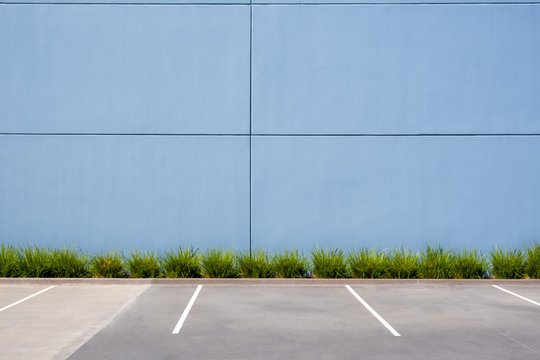 Empty parking spaces against clean concrete wall of an industrial building with pach of grass and copy space