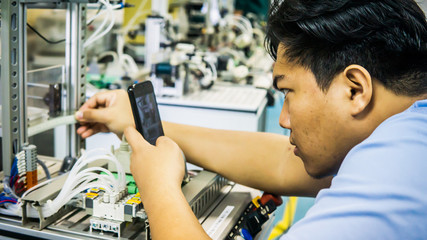 A young Malay engineering student working using a smartphone taking photo of automation machine system.