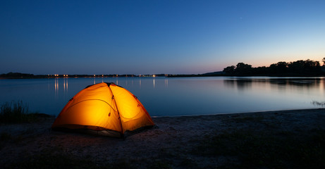 Orange interior lit tent on a lake at dusk
