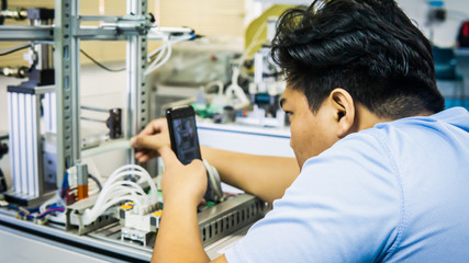 A young Malay engineering student working using a smartphone taking photo of automation machine system.