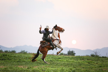 Mon riding horse against sunset with holding gun