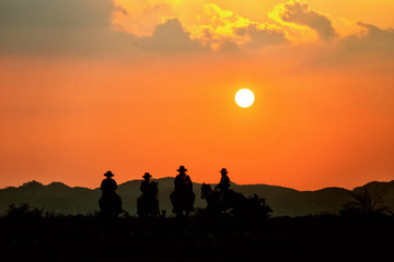 silhouette of four cowboy riding horse against sunset sky