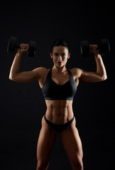 Fototapeta na wymiar Athletic woman in black top doing exercises with dumbbells.