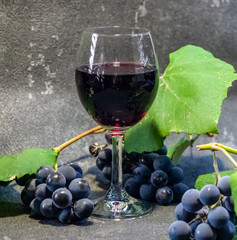 Grapes in a glass with wine on a black background. Grones of grapes with green leaves..