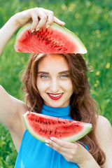 Cheerful girl is holding two slices of watermelon in front of her face. Pretty woman holds two...