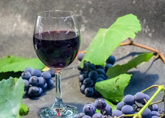Grapes in a glass with wine on a black background. Grones of grapes with green leaves..