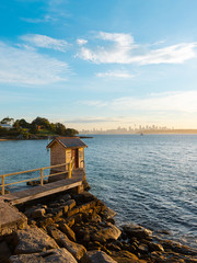 Sunset view over Camp Cove little hut with Sydney skyline on the distance.