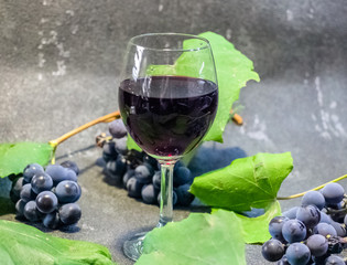Grapes in a glass with wine on a black background. Grones of grapes with green leaves..