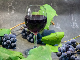 Grapes in a glass with wine on a black background. Grones of grapes with green leaves..