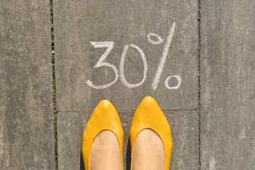 Text 30 percent written on gray pavement with woman legs, view from above