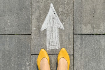 Arrow sign painted on gray sidewalk with womens legs, top view
