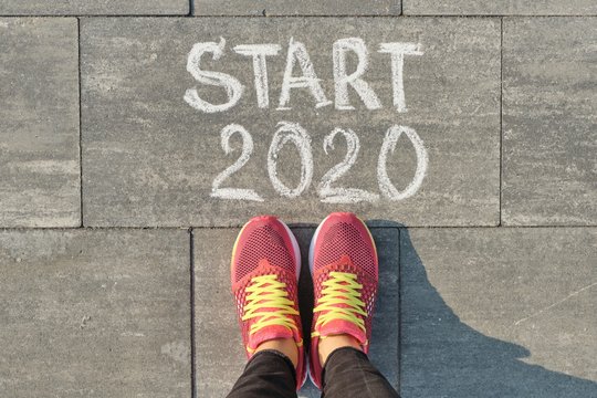 Start 2020, text on gray sidewalk with woman legs in sneakers, top view