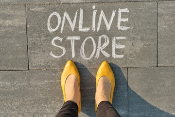 Word online store written on gray sidewalk with women legs, top view