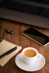  Laptop (notebook) mobile phone (smartphone) and notepad with pen on old wooden table. Work place modern.Cup of coffee