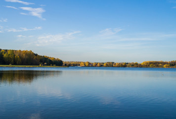 Beautiful blue lake with clear sky. Autumn yellow forest in the distance on the horizon.