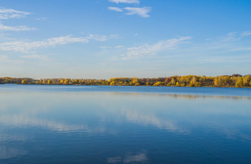 Beautiful blue lake with clear sky. Autumn yellow forest in the distance on the horizon.