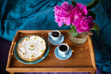 Breakfast in bed. Beautiful light from the window-peonies, cheesecake and two cups of coffee on a wooden tray