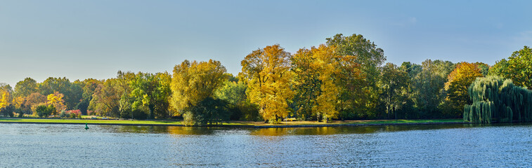 Herbstliches Panorama mit heller Sonne, die durch die B&auml;ume scheint und Reflexionen oder Spiegelungen im Wasser