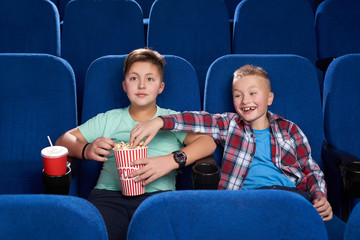 Cunning boy stealing popcorn while friend watching film