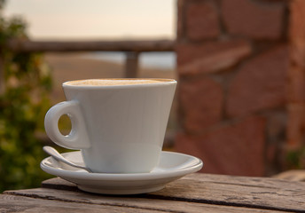 A cappuccino Cup with saucer and spoon sits on an old wooden table outside
