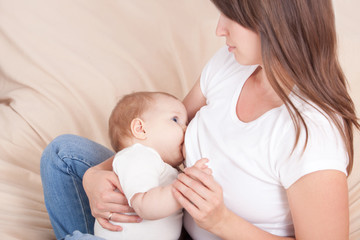 A young woman feeds the baby's chest, sitting on the bed