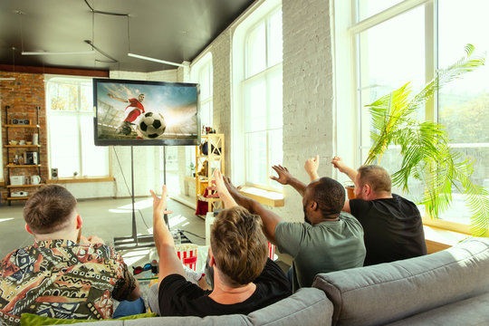 Group of friends watching game on TV at home. Sport fans spending time and having fun together. Emotional, expressive, exciting game. Cheer for favorite football or soccer team, friendship, weekend.
