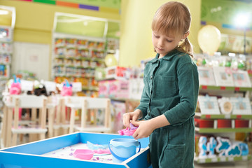 Kid playing with small sandbox and set of toys in shop.