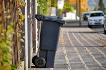 Black garbage bin for residual waste standing on the pavement in a residential area on a sunny autumn day in Germany