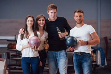 Posing for the camera. Young cheerful friends have fun in bowling club at their weekends