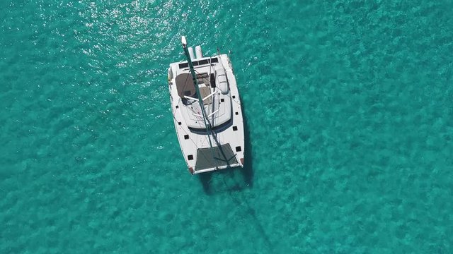 Aerial View of the White Sailing Catamaran Yacht in summer. Beautiful Weather with Calm Mirror Like Sea and Sun Shining.