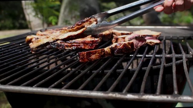 Delicious BBQ Ribs being turned from one side to the other. Pan shot