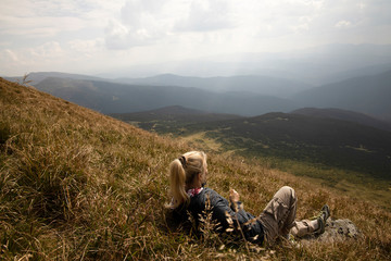 Fototapeta premium Tourist girl resting in the mountains. Tourist girl lying on the grass in the mountains. Stylish traveler woman lying on grass and relaxing in mountains. Travel concept.