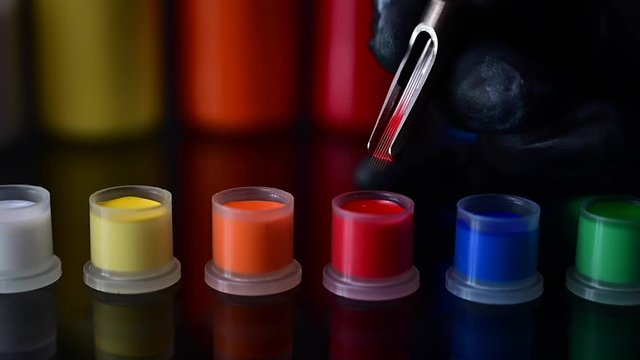 Closeup of moving tattoo needle hovering over caps filled with tattoo ink of different color 