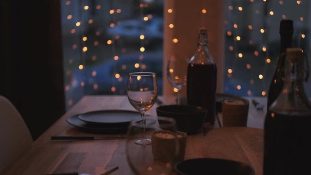 Served table at home in the living room against the window. Evening dim light. Garlands are hanging on the window. Preparing for the celebration. Christmas party.