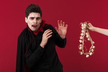 Image of young vampire man in halloween costume being scared of garlic