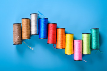 Sewing kit: scissors, measuring tape, thimbles, threads and buttons. Composition with threads and accessories on blue background Colored coils on blue background, place for text