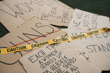 Caution tape on the paper. Group of banners with different feminist quotes lying on the ground