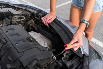woman near car hood. young girl in covered parking, stands near car with raised engine compartment hood, checks engine oil level in engine, inspects feeler gauge - obrazy, fototapety, plakaty