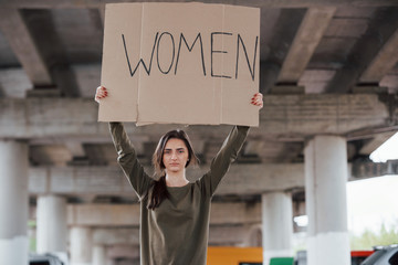 Standing alone. Pretty girl in casual clothes with handmade feminist poster in hands