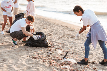 Image of kind volunteers cleaning beach from plastic with trash bags
