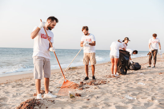 Image of confident volunteers cleaning beach from plastic with trash bags