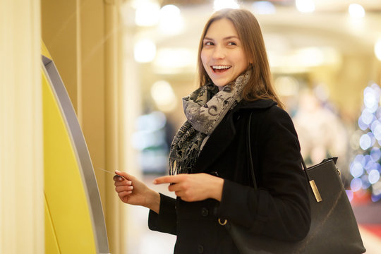 Photo of young woman with bank card at ATM on blurred background