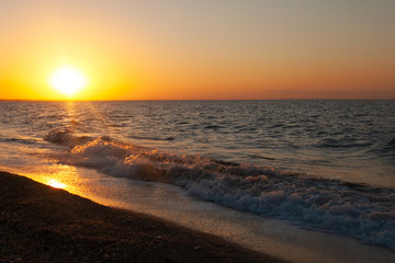 Fototapeta premium Sunset over the sea. Sea wave rolls ashore. The horizon is flooded with sunlight ..