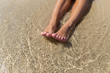 Top view of naked tanned female feet in the sand on the beach, point of view of feet in the sand with sea foam ocean summer background-image, relaxing on the ocean beach, feet on the sea sand-image