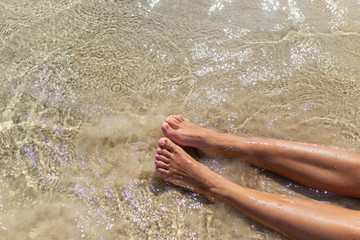 Top view of naked tanned female feet in the sand on the beach, point of view of feet in the sand with sea foam ocean summer background-image, relaxing on the ocean beach, feet on the sea sand-image