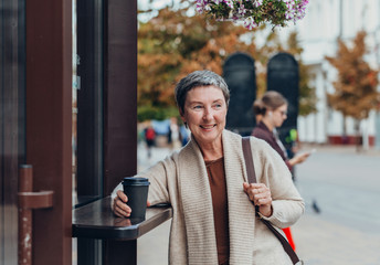 Happy stylish stylish fashionable senior woman dressed in the city streets with a glass of coffee...