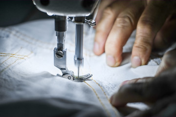 Hand of the seamstress is using a white industrial sewing machine to sew cloth.